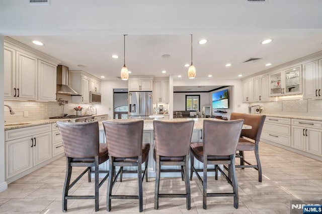 kitchen featuring visible vents, decorative backsplash, wall chimney exhaust hood, a sink, and appliances with stainless steel finishes