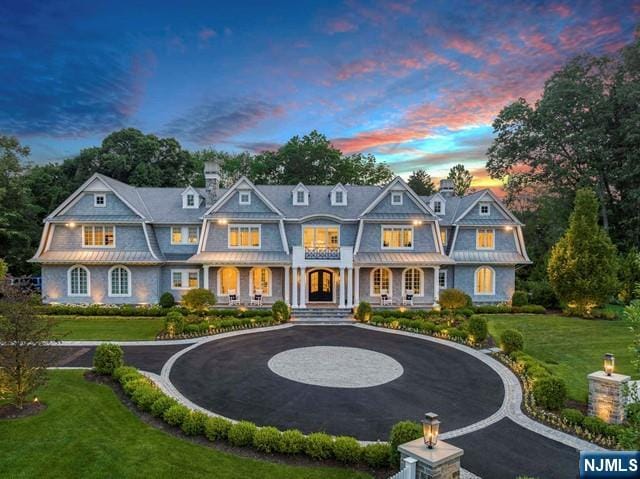 shingle-style home with curved driveway, a yard, and covered porch
