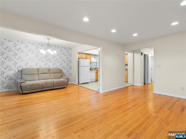 living room featuring light wood-style floors, baseboards, an accent wall, and wallpapered walls
