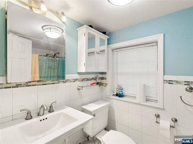 bathroom with a sink, a shower with shower curtain, toilet, and tile walls