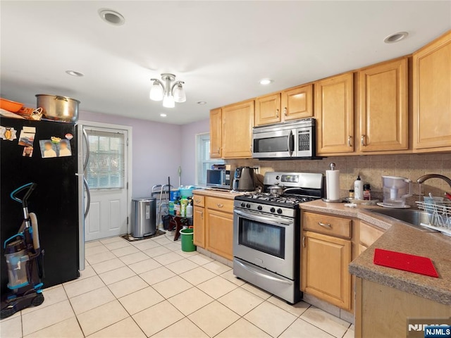kitchen with decorative backsplash, appliances with stainless steel finishes, a sink, light tile patterned floors, and light brown cabinets