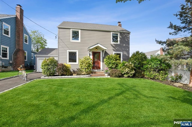 colonial house with a garage, aphalt driveway, fence, a front yard, and a chimney