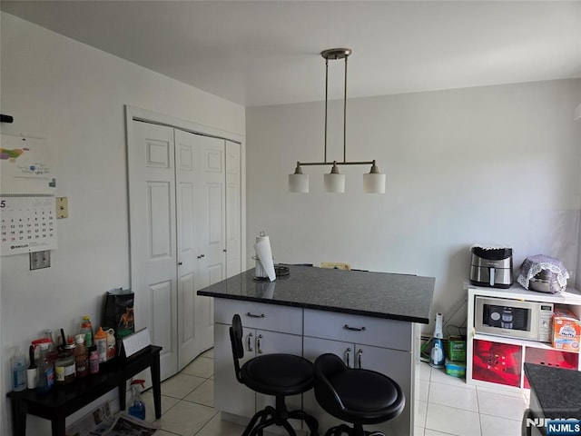 kitchen with decorative light fixtures, stainless steel microwave, a kitchen island, and light tile patterned floors