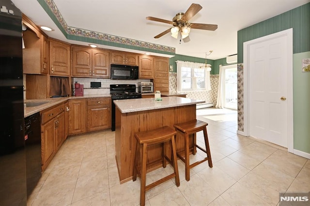 kitchen featuring ceiling fan, decorative backsplash, a center island, brown cabinets, and black appliances