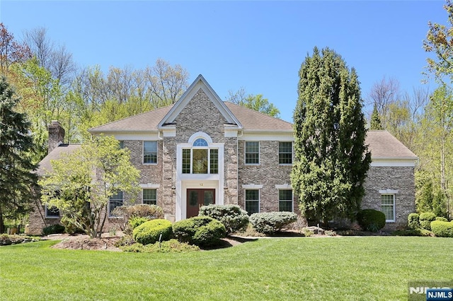 view of front of property with a front yard, a chimney, brick siding, and french doors