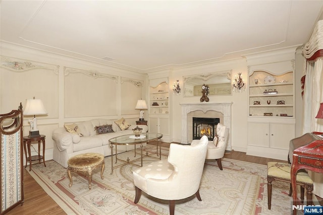 living room with crown molding, built in shelves, a fireplace, and wood finished floors