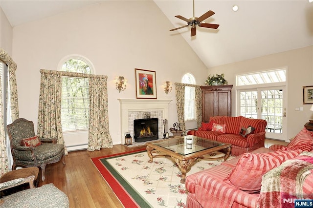 living room with high vaulted ceiling, a ceiling fan, wood finished floors, a fireplace, and a baseboard radiator