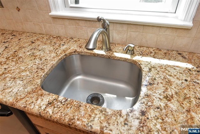 room details with a sink, light stone countertops, and tasteful backsplash