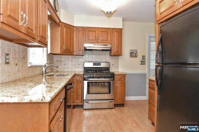 kitchen featuring a sink, brown cabinetry, light wood-style flooring, under cabinet range hood, and black appliances