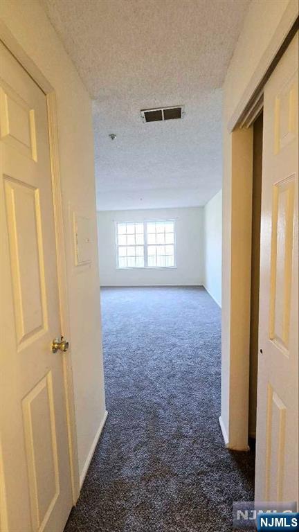 corridor with carpet floors, a textured ceiling, baseboards, and visible vents