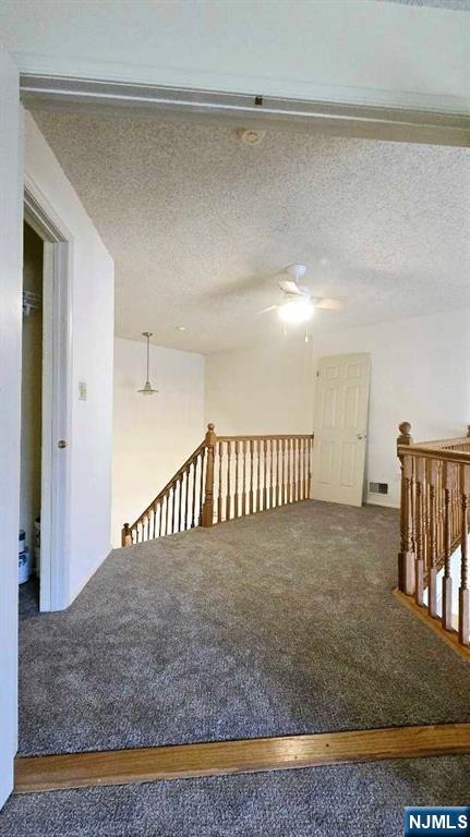 carpeted spare room featuring visible vents, a textured ceiling, and ceiling fan
