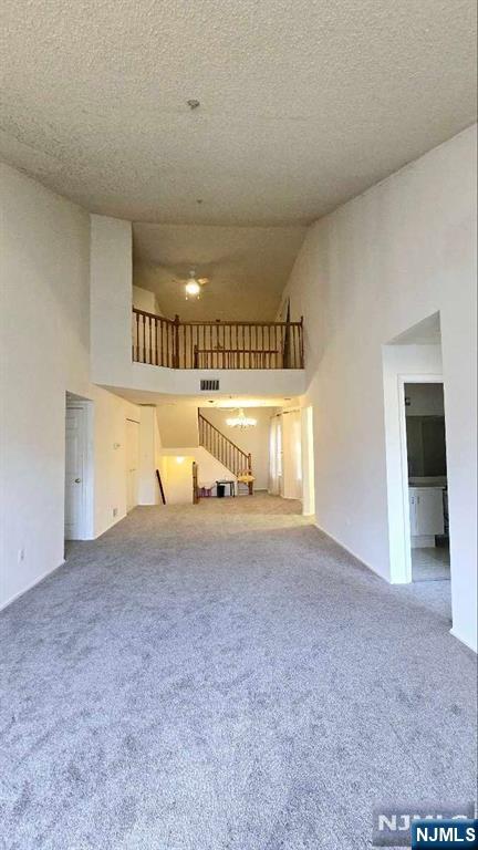 unfurnished living room with visible vents, stairs, high vaulted ceiling, a textured ceiling, and carpet