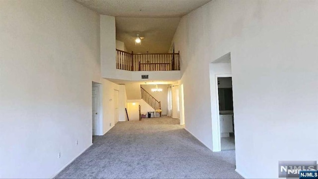 hallway featuring a high ceiling, carpet flooring, stairs, and visible vents