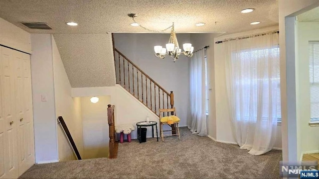 interior space with an inviting chandelier, carpet floors, a textured ceiling, and visible vents