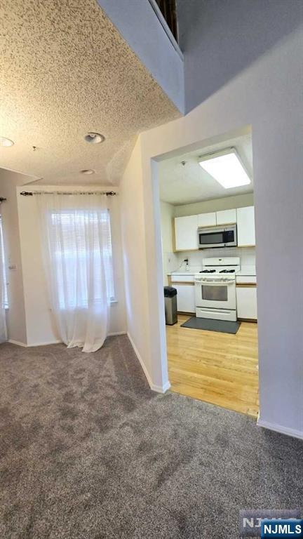 interior space with a textured ceiling, baseboards, and light carpet