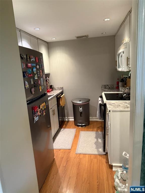 kitchen with freestanding refrigerator, light wood-style floors, range with electric stovetop, white microwave, and light countertops