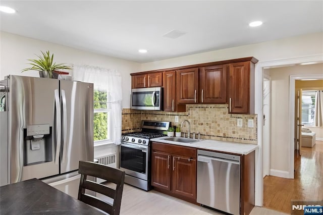kitchen featuring stainless steel appliances, a sink, light wood-type flooring, backsplash, and recessed lighting