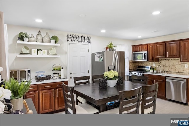 kitchen featuring appliances with stainless steel finishes, a sink, light countertops, decorative backsplash, and open shelves