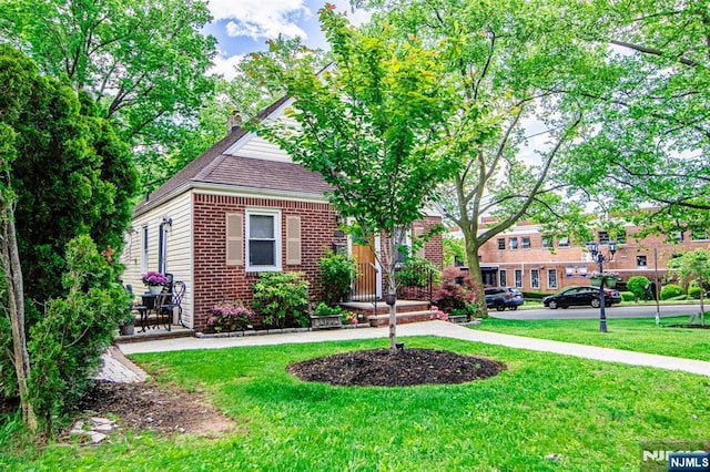 view of front of property with brick siding, a front yard, a chimney, and a shingled roof
