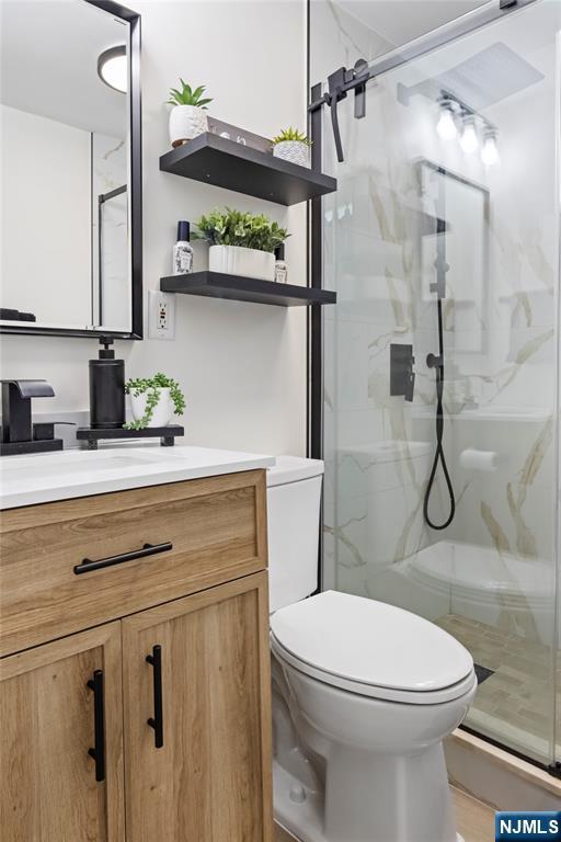 bathroom with a marble finish shower, toilet, and vanity
