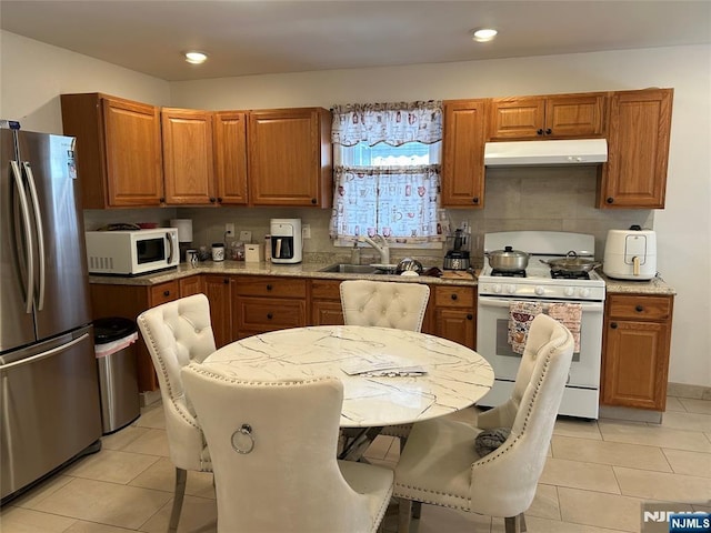 kitchen featuring white appliances, brown cabinetry, recessed lighting, light tile patterned floors, and under cabinet range hood