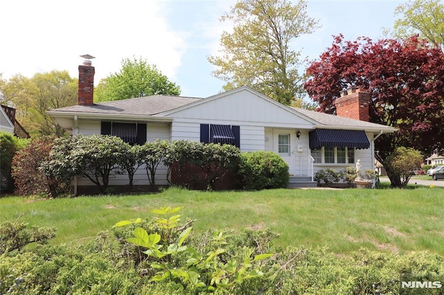 view of front of house with board and batten siding, a front yard, and a chimney