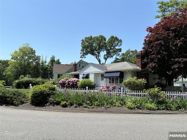 view of front of property with board and batten siding, a fenced front yard, and a chimney