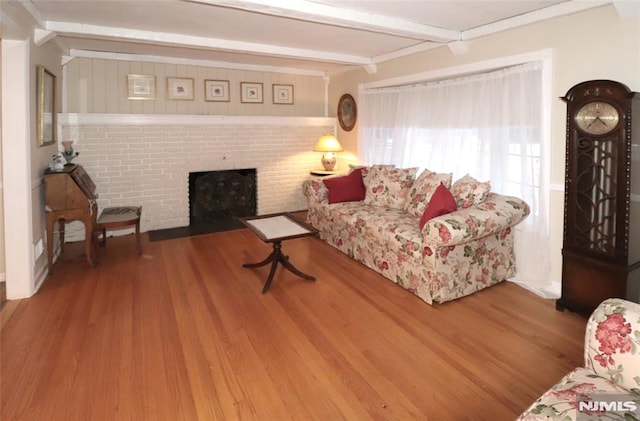 living area featuring beamed ceiling, a brick fireplace, and wood finished floors