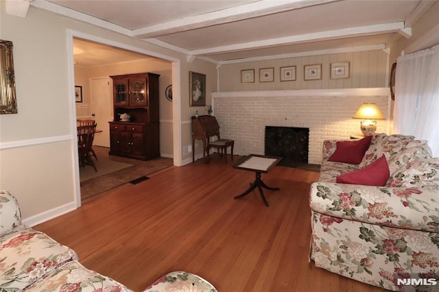 living room featuring baseboards, beam ceiling, a brick fireplace, and wood finished floors