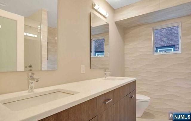 full bath featuring double vanity, a sink, toilet, and tile walls