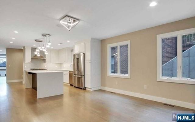 kitchen featuring baseboards, freestanding refrigerator, a kitchen island, and wood finished floors