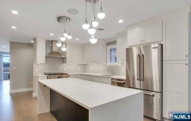kitchen featuring a sink, tasteful backsplash, stainless steel appliances, and wall chimney exhaust hood
