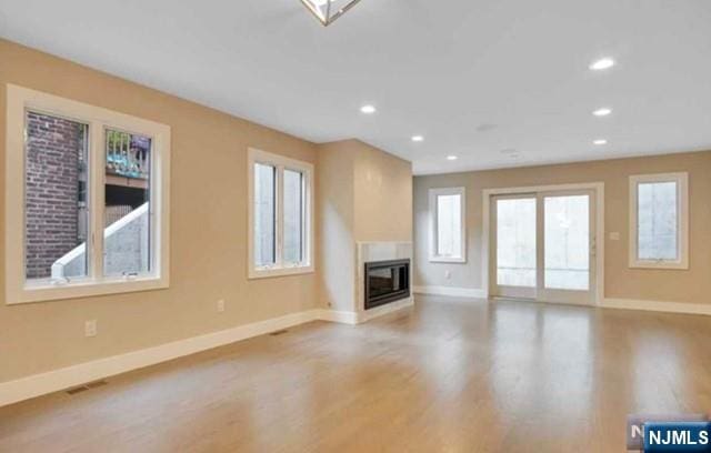 unfurnished living room featuring recessed lighting, baseboards, a glass covered fireplace, and light wood-type flooring