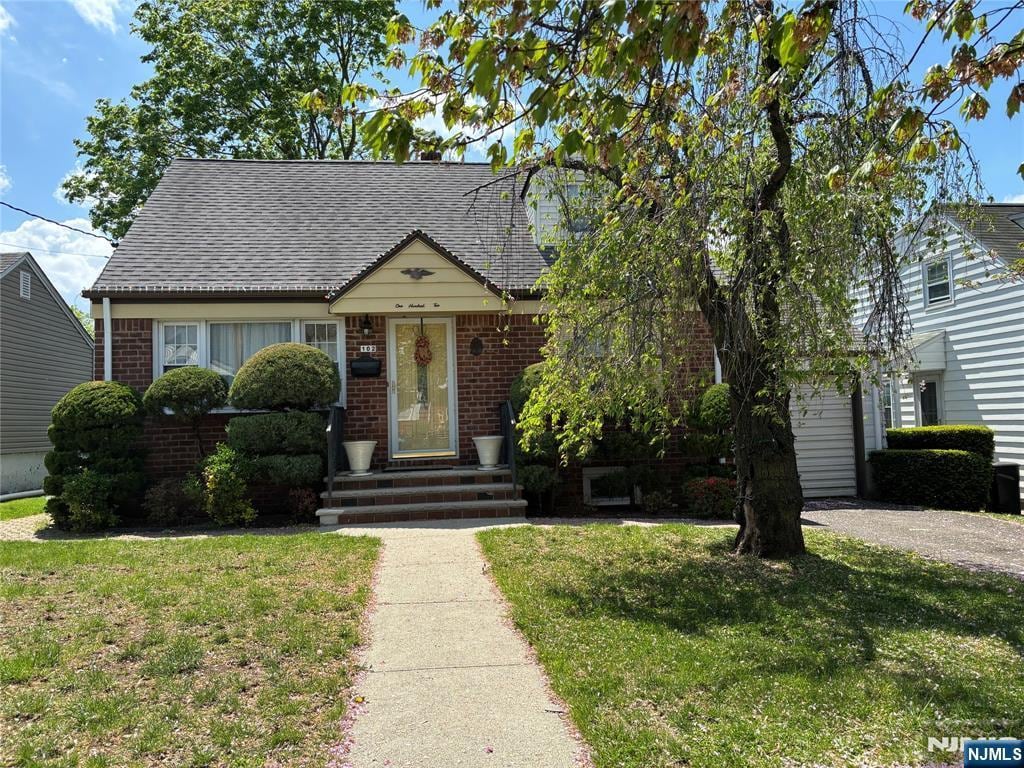 view of front of property with brick siding, a front lawn, and roof with shingles