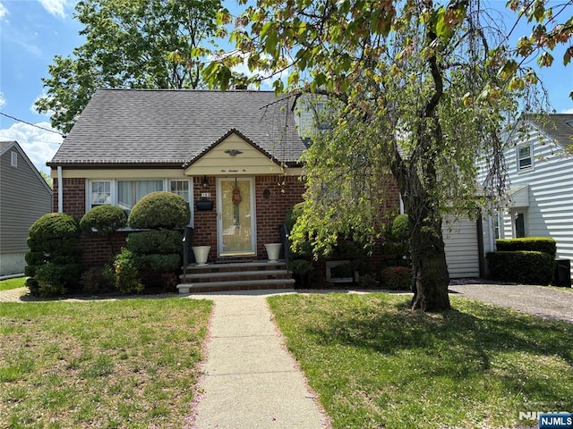 view of front of property with brick siding, a front lawn, and roof with shingles