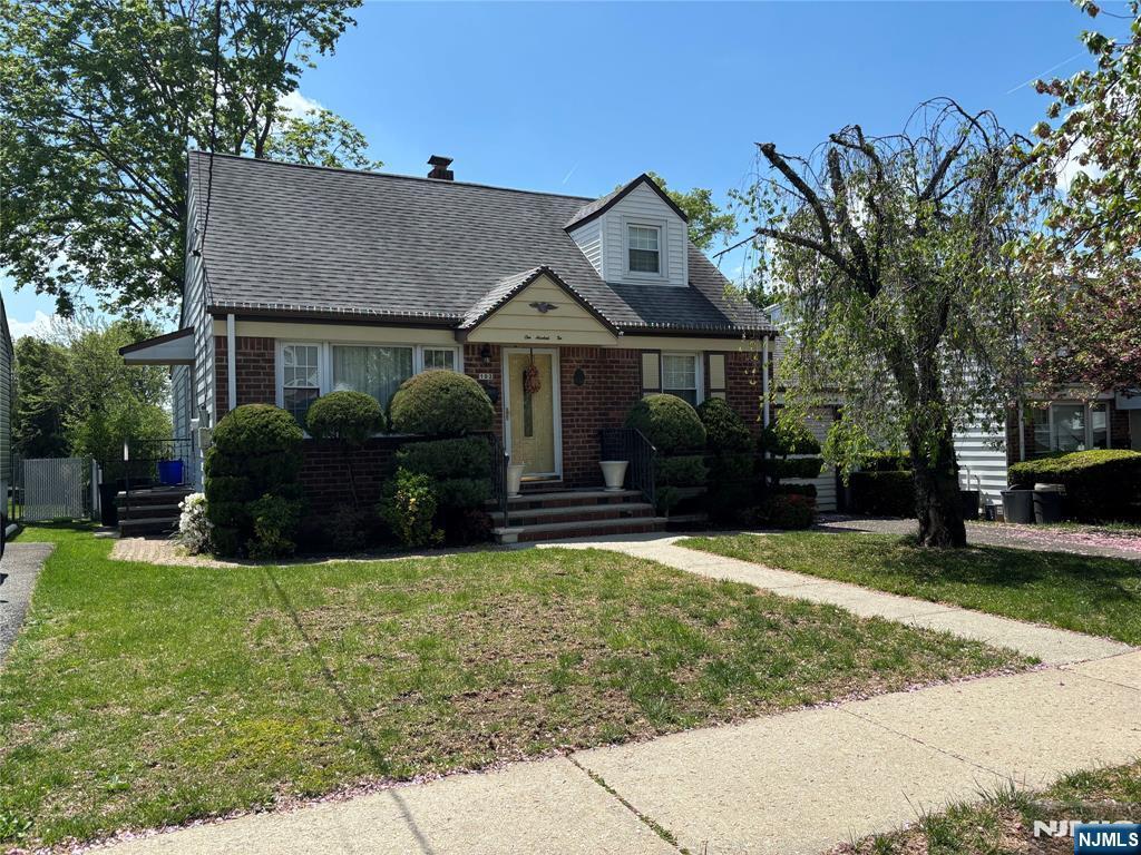 cape cod house with brick siding, a shingled roof, and a front yard