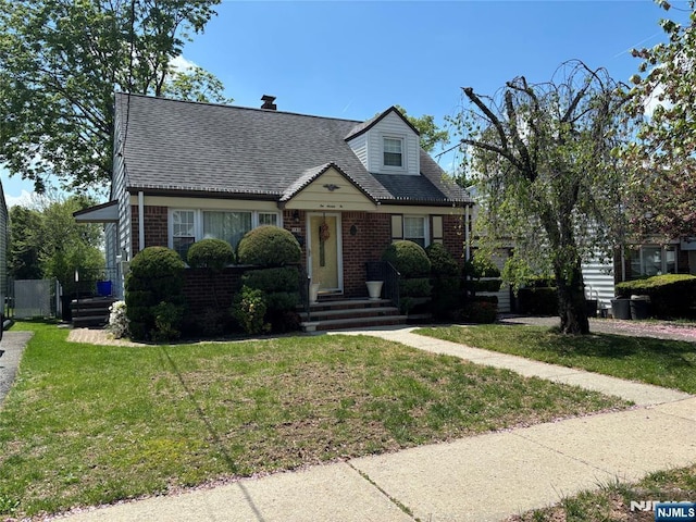 cape cod house with brick siding, a shingled roof, and a front yard