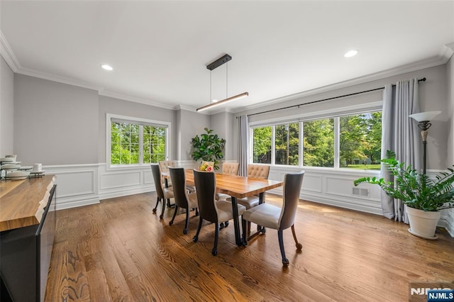 dining area featuring ornamental molding, wood finished floors, recessed lighting, wainscoting, and a decorative wall