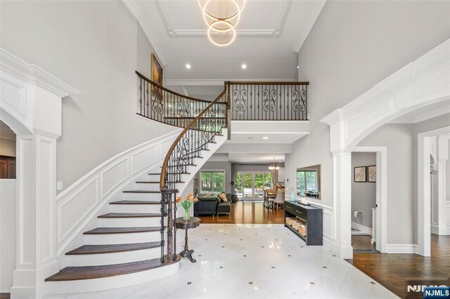 entrance foyer featuring a chandelier, stairway, decorative columns, arched walkways, and a towering ceiling