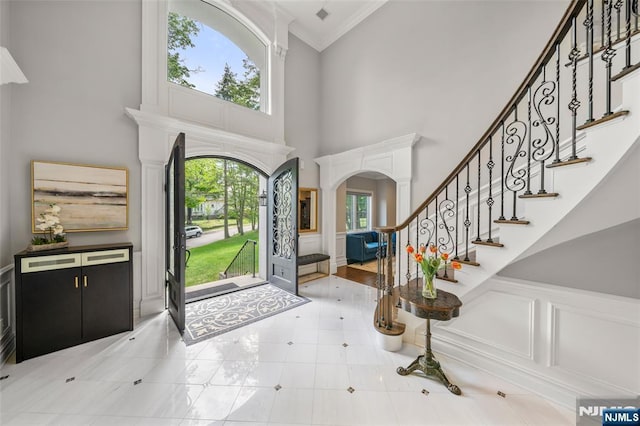 tiled entryway with a high ceiling, arched walkways, ornamental molding, stairway, and a decorative wall