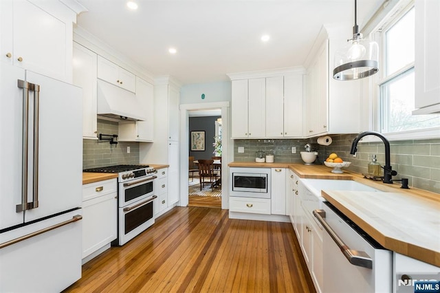 kitchen featuring high end appliances, tasteful backsplash, custom range hood, a sink, and wood counters