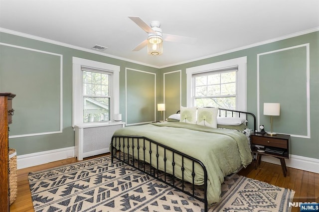 bedroom with crown molding, radiator heating unit, baseboards, wood finished floors, and visible vents
