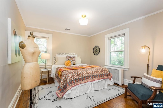 bedroom featuring radiator heating unit, multiple windows, wood finished floors, and visible vents
