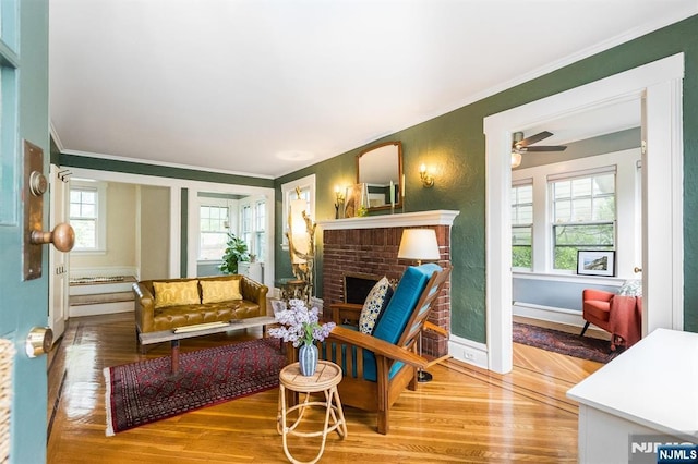 living room with crown molding, a fireplace, a ceiling fan, and wood finished floors