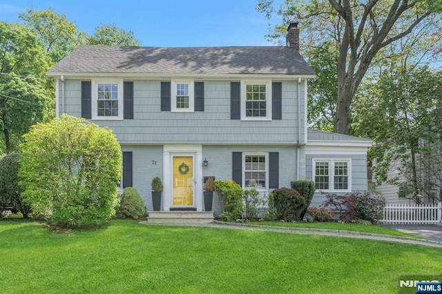 colonial house featuring brick siding, a chimney, and a front yard