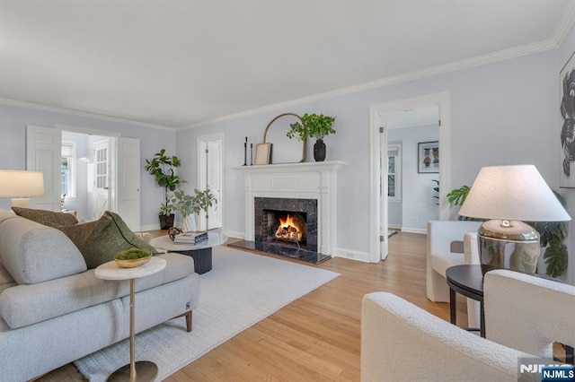 living area with a premium fireplace, ornamental molding, light wood-style flooring, and baseboards