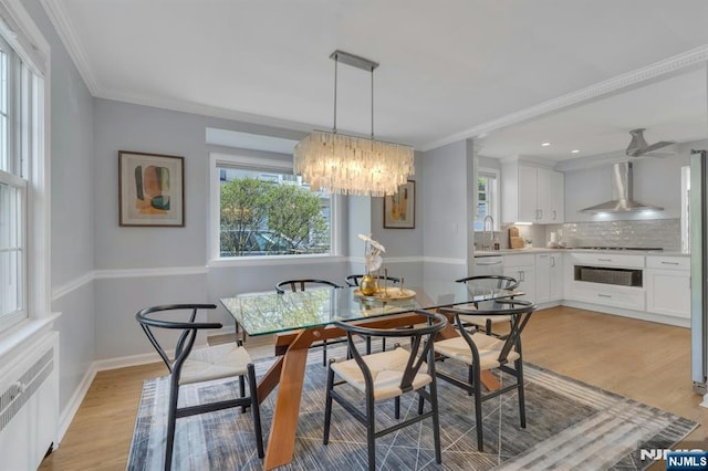 dining area featuring radiator heating unit, ornamental molding, light wood-type flooring, a chandelier, and baseboards