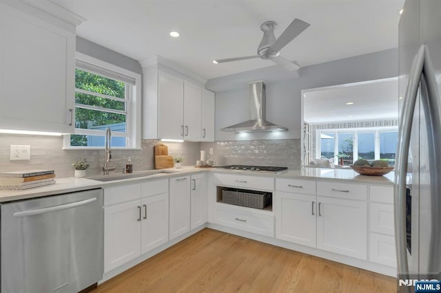 kitchen with light countertops, a sink, white cabinetry, wall chimney range hood, and appliances with stainless steel finishes