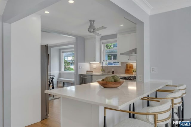 kitchen featuring a peninsula, white cabinetry, backsplash, under cabinet range hood, and appliances with stainless steel finishes