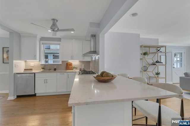kitchen featuring stainless steel appliances, white cabinets, a ceiling fan, and wall chimney exhaust hood